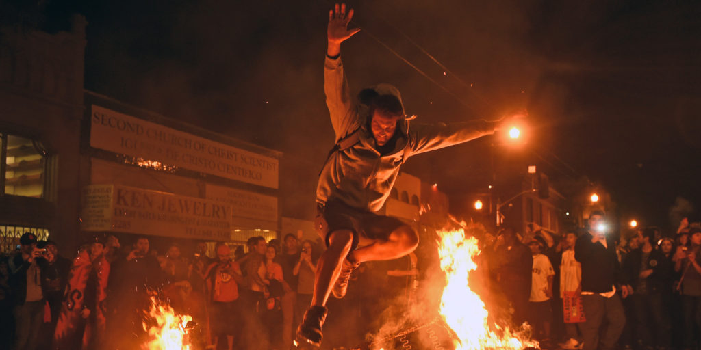 A man jumps over some debris that has been set on fire in the Mission district after the San Francisco Giants beat the Kansas City Royals to win the World Series on Wednesday, Oct. 29, 2014, in San Francisco. (AP Photo/Noah Berger)